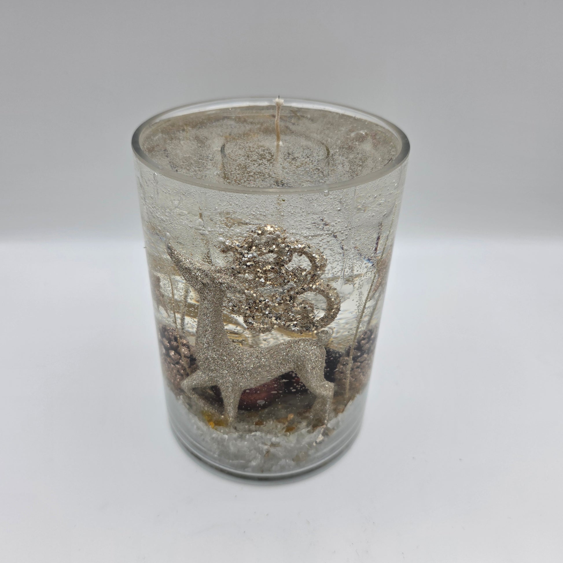 Handcrafted golden reindeer candle in a clear glass container with winter accents