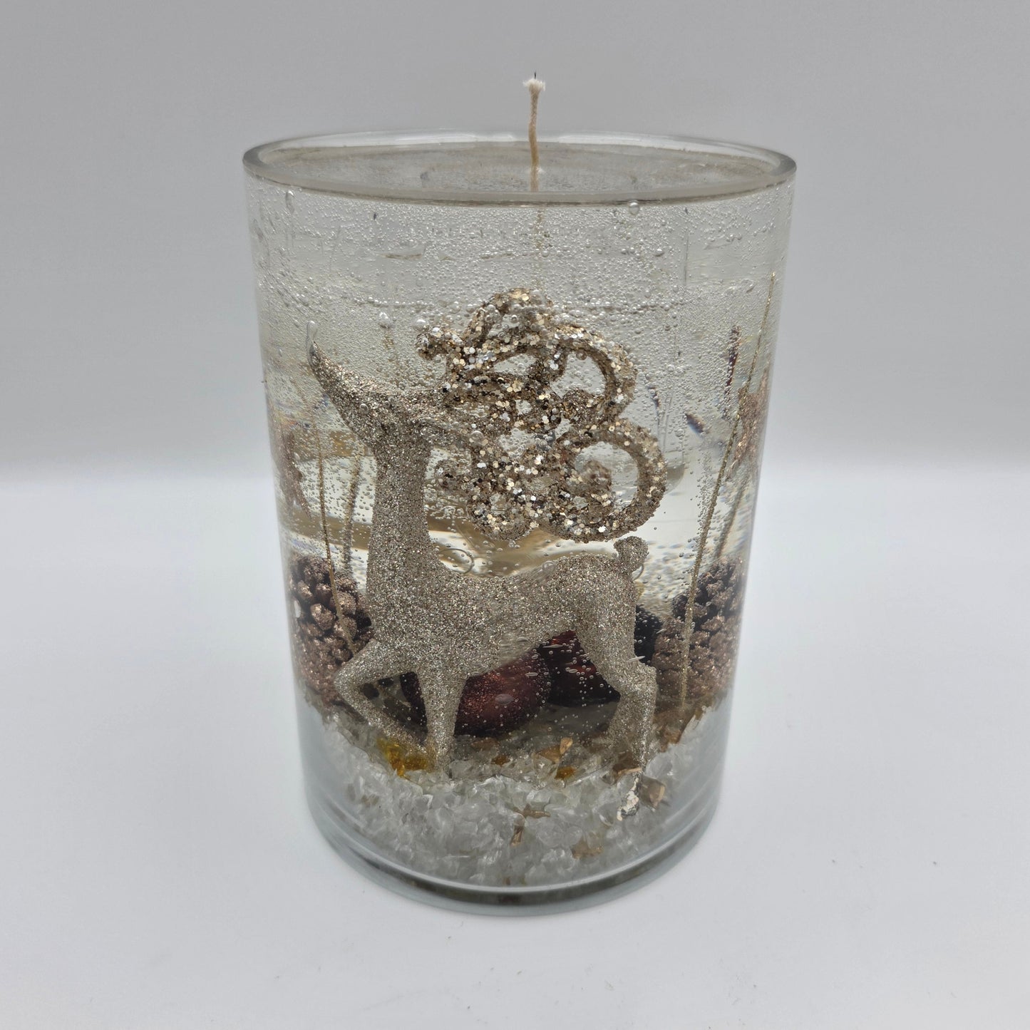Handcrafted golden reindeer candle in a clear glass container with winter accents.