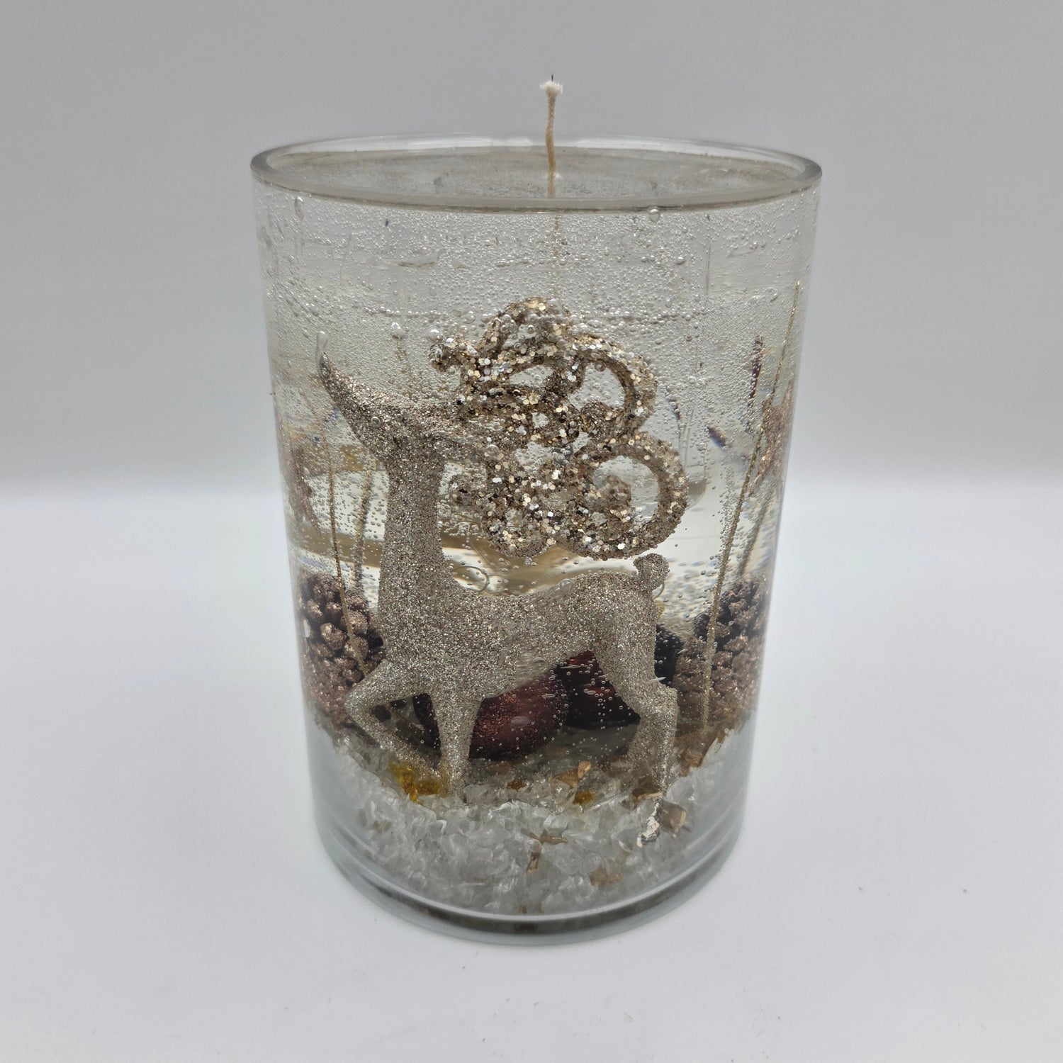 Handcrafted golden reindeer candle in a clear glass container with winter accents.