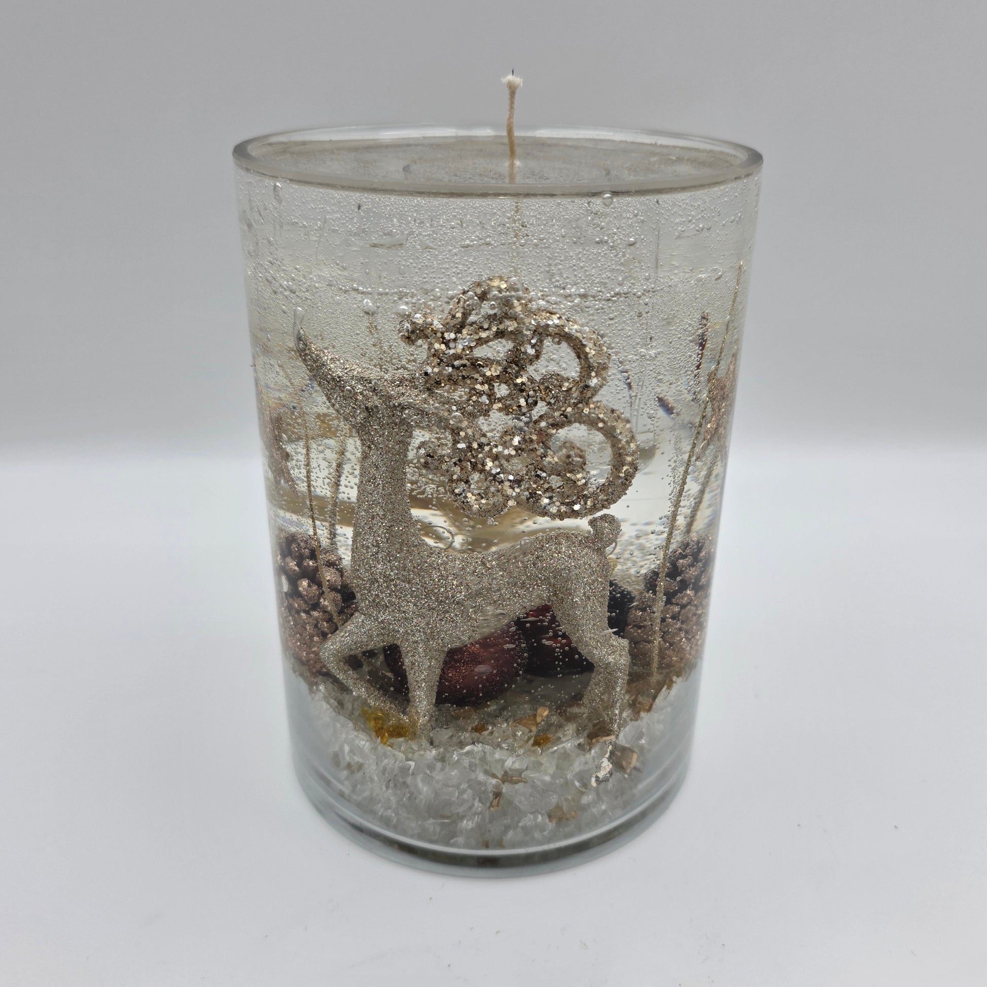 Handcrafted golden reindeer candle in a clear glass container with winter accents.